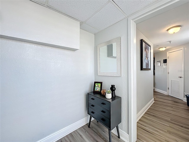 hallway featuring a paneled ceiling, baseboards, visible vents, and light wood-type flooring