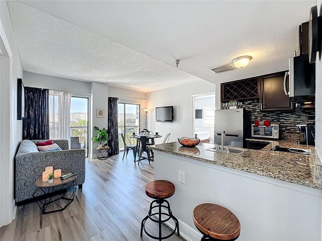 kitchen with freestanding refrigerator, a peninsula, a textured ceiling, light wood finished floors, and stone counters