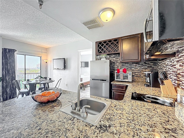 kitchen with visible vents, a sink, a textured ceiling, stainless steel appliances, and decorative backsplash