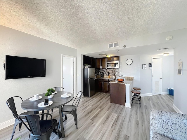 dining area featuring light wood-type flooring, baseboards, visible vents, and a textured ceiling