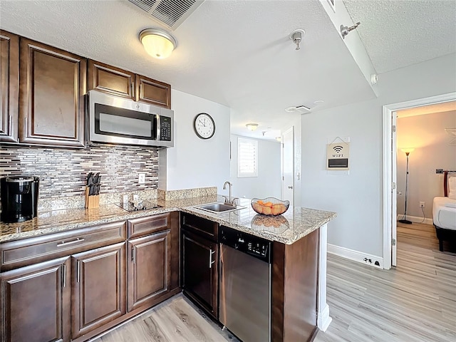 kitchen featuring tasteful backsplash, a sink, a peninsula, light wood-style floors, and stainless steel appliances