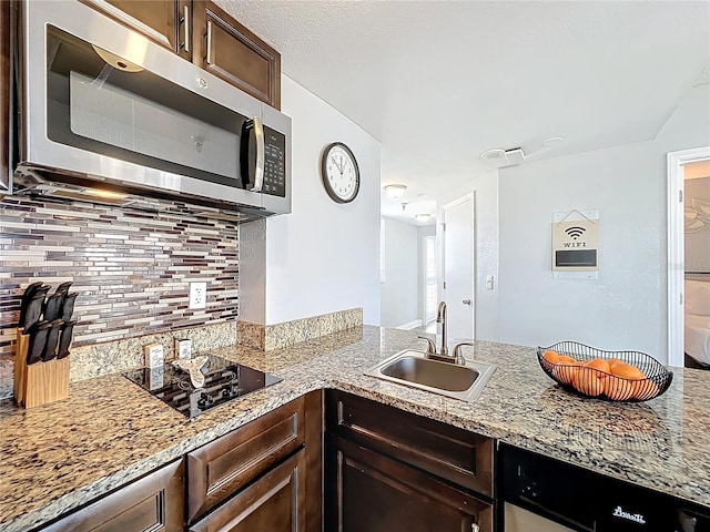 kitchen featuring dark brown cabinetry, stainless steel microwave, a sink, backsplash, and black cooktop