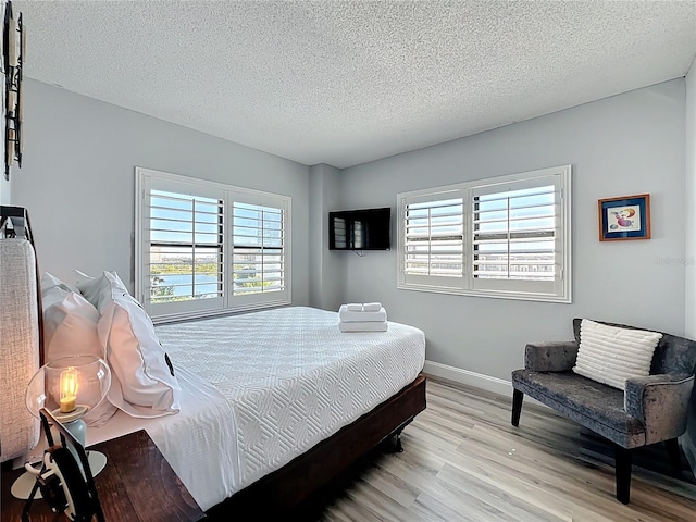 bedroom with a textured ceiling, light wood finished floors, and baseboards