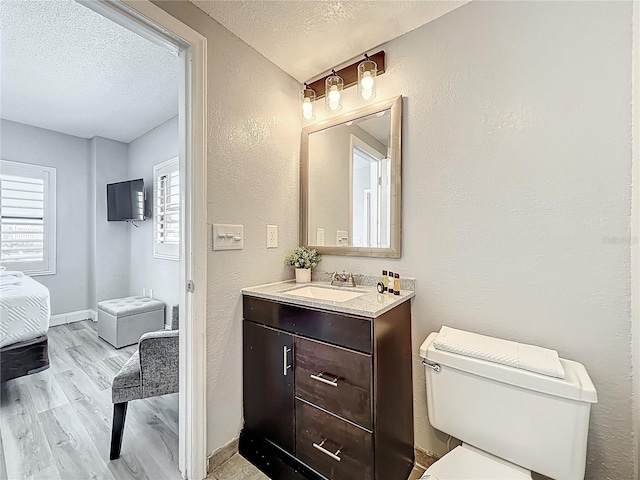 bathroom featuring a textured ceiling, vanity, toilet, wood finished floors, and a textured wall