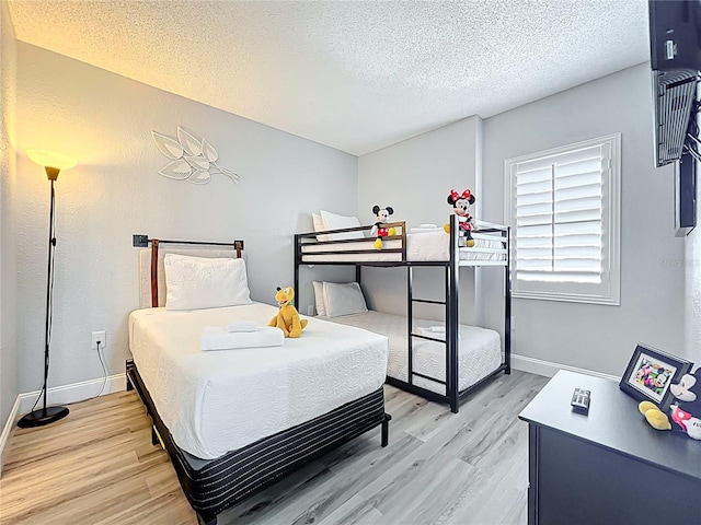bedroom with light wood-type flooring, baseboards, and a textured ceiling