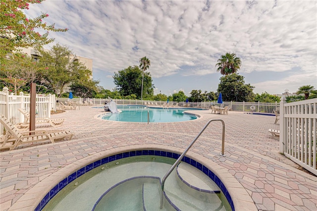 community pool with a patio area, fence, and a hot tub