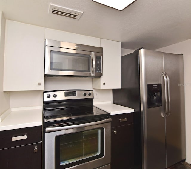 kitchen with stainless steel appliances, a textured ceiling, and white cabinets