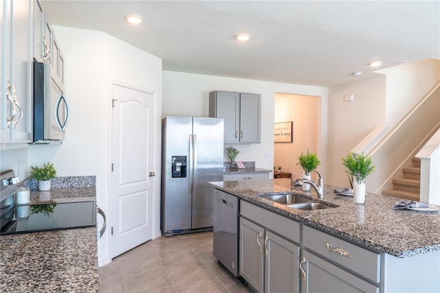 kitchen with stainless steel appliances, dark stone counters, sink, an island with sink, and light tile patterned flooring