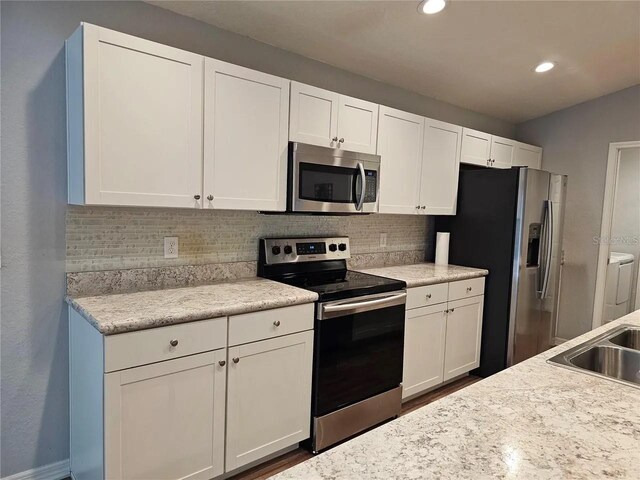 kitchen featuring decorative backsplash, appliances with stainless steel finishes, washing machine and dryer, and white cabinets