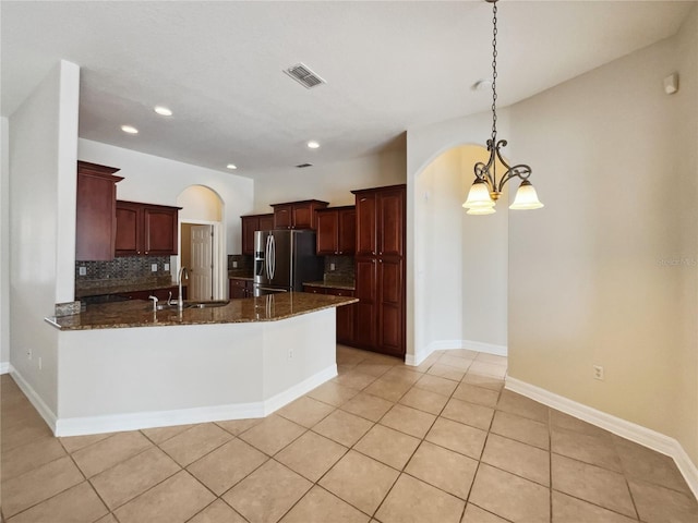 kitchen featuring sink, stainless steel fridge with ice dispenser, backsplash, dark stone counters, and pendant lighting