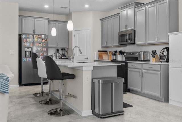 kitchen with gray cabinetry, appliances with stainless steel finishes, sink, an island with sink, and decorative light fixtures