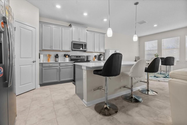 kitchen featuring gray cabinets, a kitchen island, appliances with stainless steel finishes, and pendant lighting