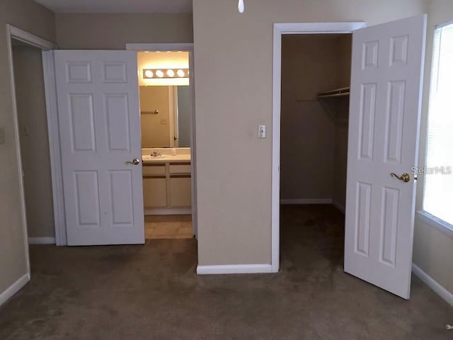 unfurnished bedroom with a closet, a spacious closet, ensuite bath, and dark colored carpet