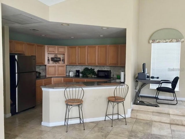 kitchen with tasteful backsplash, stainless steel refrigerator, a breakfast bar area, and kitchen peninsula