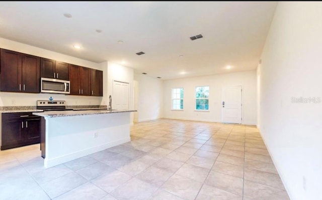 kitchen featuring range with electric cooktop, light stone countertops, dark brown cabinetry, light tile patterned floors, and a center island with sink