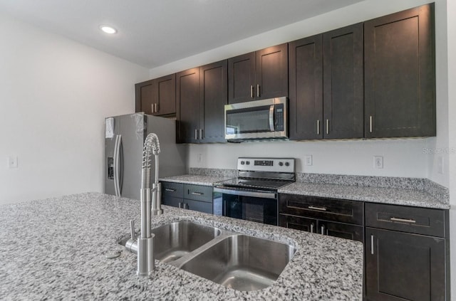 kitchen featuring light stone counters, stainless steel appliances, dark brown cabinets, and sink