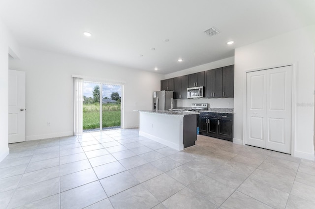 kitchen with a center island with sink, light stone countertops, stainless steel appliances, and light tile patterned floors