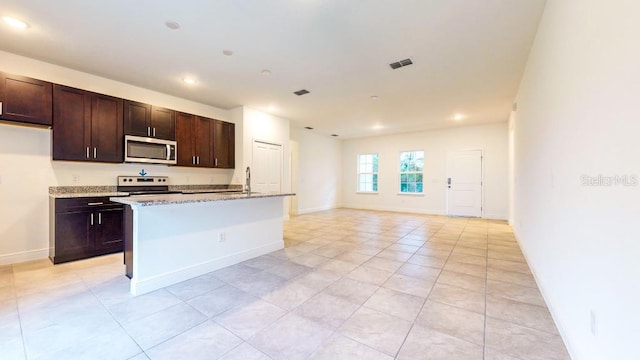 kitchen with dark brown cabinetry, a kitchen island with sink, light stone countertops, and range with electric stovetop