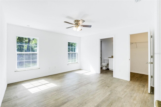 unfurnished bedroom featuring a closet, light hardwood / wood-style flooring, ensuite bath, a spacious closet, and ceiling fan