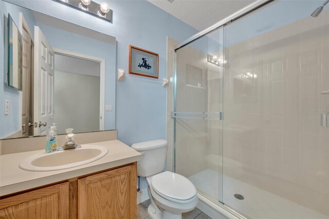 bathroom with a textured ceiling, a shower with shower door, toilet, vanity, and tile patterned flooring