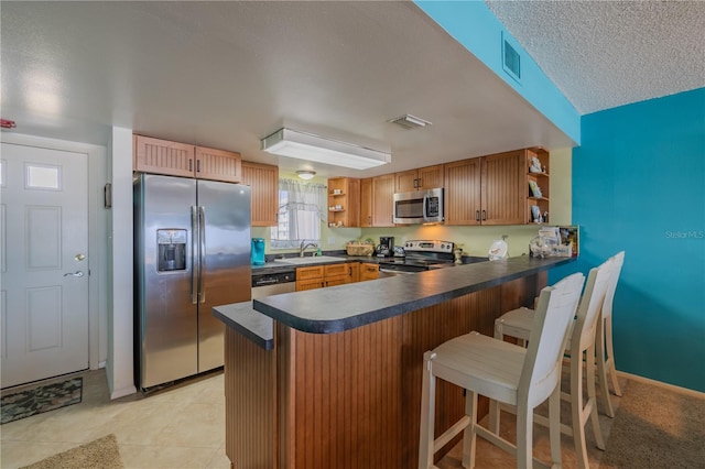 kitchen with kitchen peninsula, sink, light tile patterned floors, appliances with stainless steel finishes, and a textured ceiling