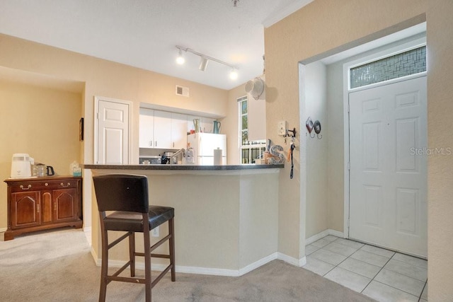 kitchen with light carpet, kitchen peninsula, white cabinets, a breakfast bar, and white fridge