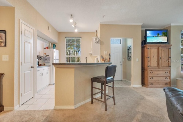 kitchen with kitchen peninsula, a kitchen bar, ornamental molding, white fridge, and light colored carpet