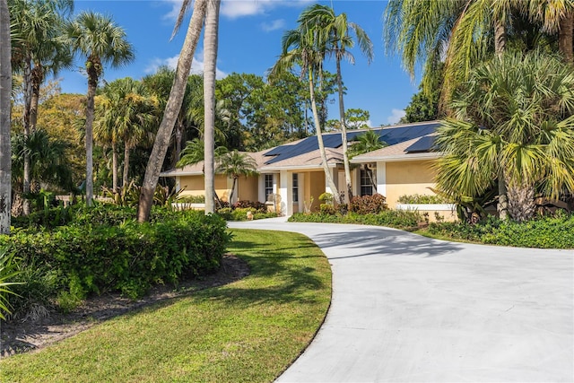 single story home featuring solar panels and a front lawn