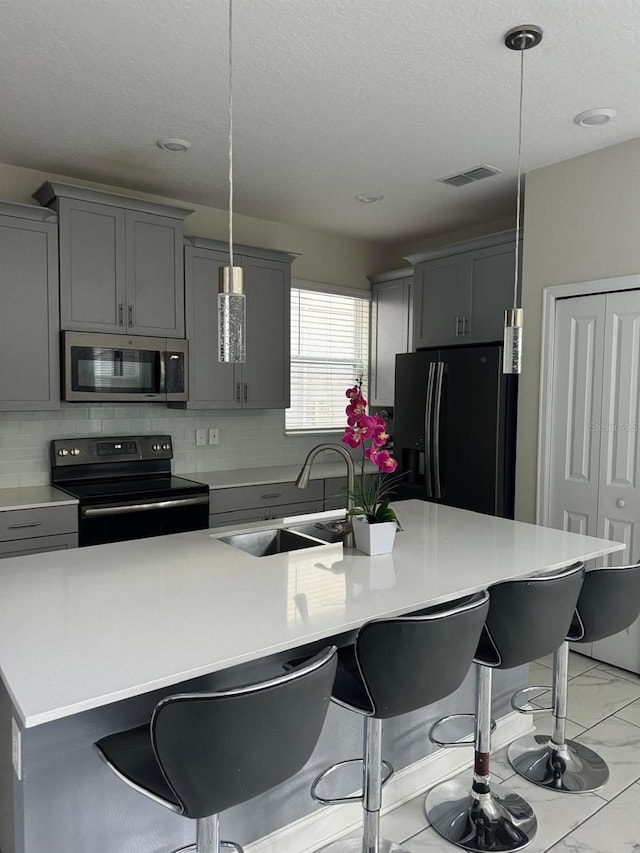 kitchen with a kitchen island with sink, black appliances, hanging light fixtures, and sink