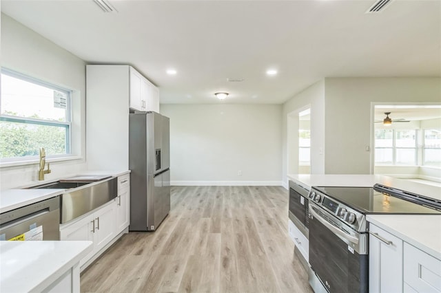 kitchen featuring appliances with stainless steel finishes, light wood-type flooring, white cabinetry, and plenty of natural light