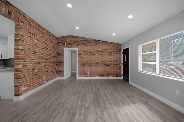 unfurnished living room with lofted ceiling, brick wall, and light hardwood / wood-style flooring