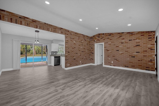 unfurnished living room featuring brick wall, light wood-type flooring, and vaulted ceiling