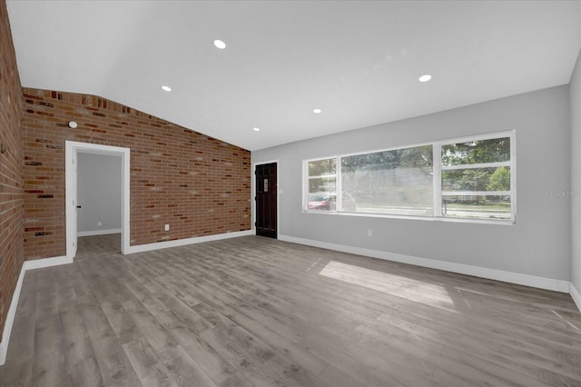 unfurnished living room featuring brick wall, light wood-type flooring, and vaulted ceiling