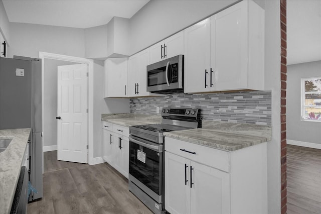 kitchen featuring appliances with stainless steel finishes, light hardwood / wood-style floors, light stone counters, white cabinets, and tasteful backsplash