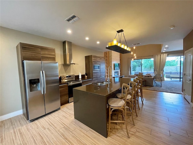 kitchen with wall chimney range hood, hanging light fixtures, appliances with stainless steel finishes, a kitchen breakfast bar, and sink