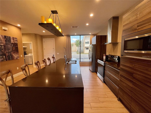 kitchen with wall chimney exhaust hood, washer / dryer, stainless steel appliances, sink, and decorative light fixtures