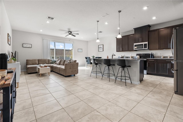 kitchen with a center island with sink, a kitchen bar, pendant lighting, appliances with stainless steel finishes, and ceiling fan