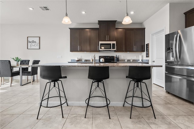 kitchen featuring a center island with sink, pendant lighting, light stone countertops, and stainless steel appliances