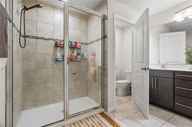 bathroom featuring toilet, a shower with shower door, vanity, and tile patterned flooring