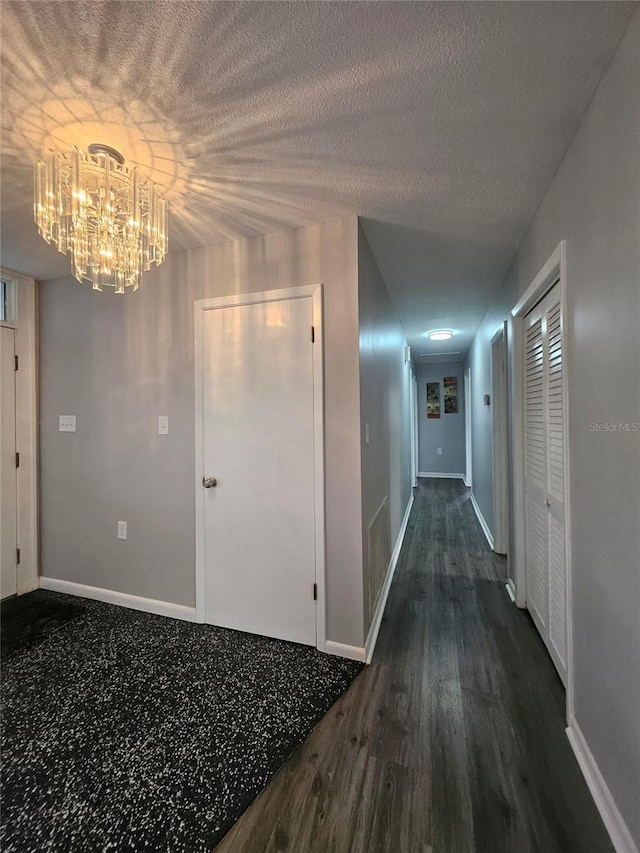 corridor with an inviting chandelier, dark hardwood / wood-style flooring, and a textured ceiling