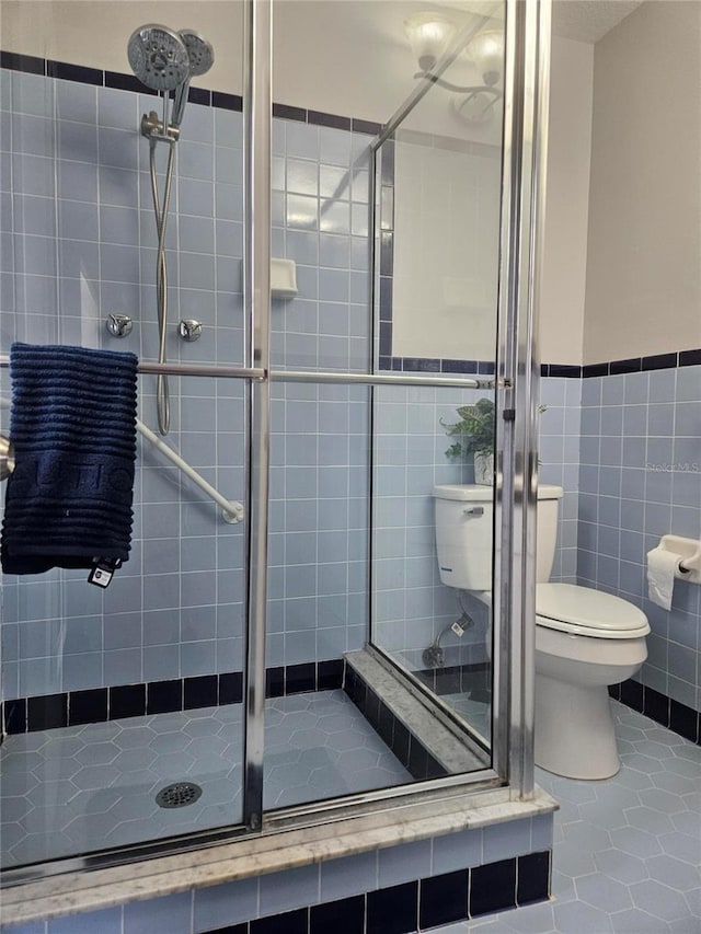 bathroom featuring tile patterned flooring, a shower with door, tile walls, and toilet