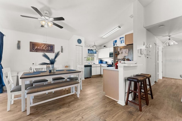 kitchen featuring vaulted ceiling, kitchen peninsula, a kitchen breakfast bar, white cabinetry, and appliances with stainless steel finishes