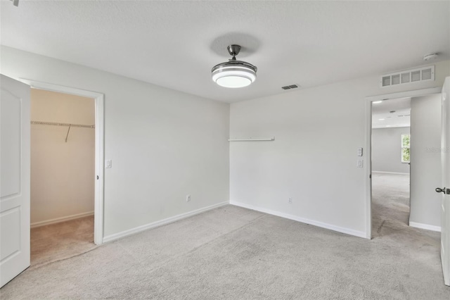 unfurnished bedroom featuring a spacious closet, light carpet, and a closet