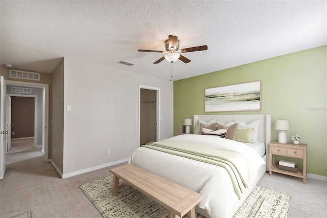 bedroom with a closet, a walk in closet, a textured ceiling, light colored carpet, and ceiling fan