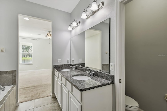 bathroom with tile patterned flooring, a relaxing tiled tub, ceiling fan, vanity, and toilet