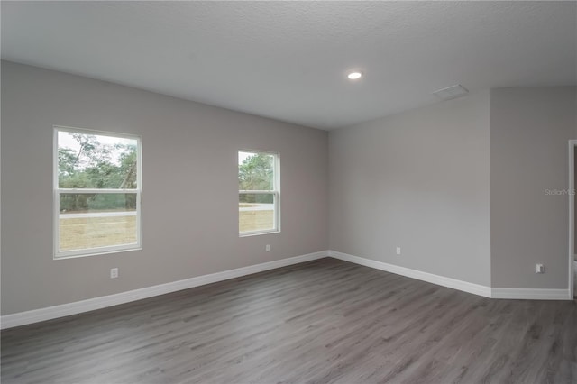 unfurnished room featuring a healthy amount of sunlight, a textured ceiling, and dark hardwood / wood-style floors