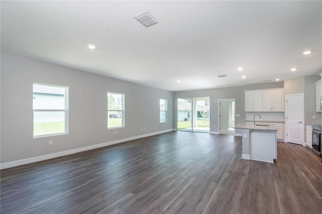 kitchen featuring a sink, visible vents, open floor plan, backsplash, and a center island with sink