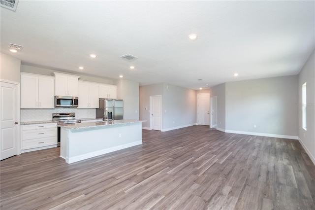 kitchen with stainless steel appliances, a kitchen island with sink, visible vents, and tasteful backsplash