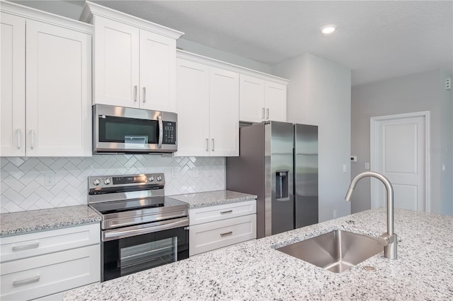 kitchen featuring light stone counters, a sink, stainless steel appliances, white cabinetry, and backsplash