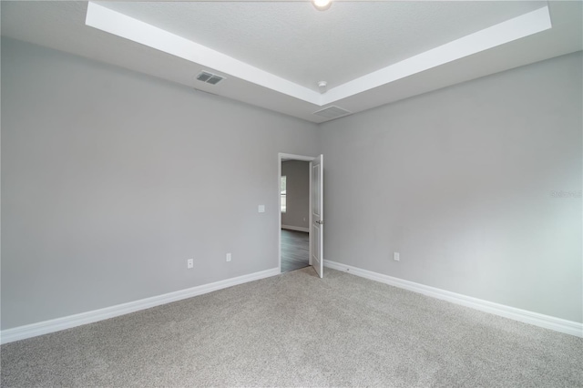 spare room with a tray ceiling, carpet, visible vents, and baseboards